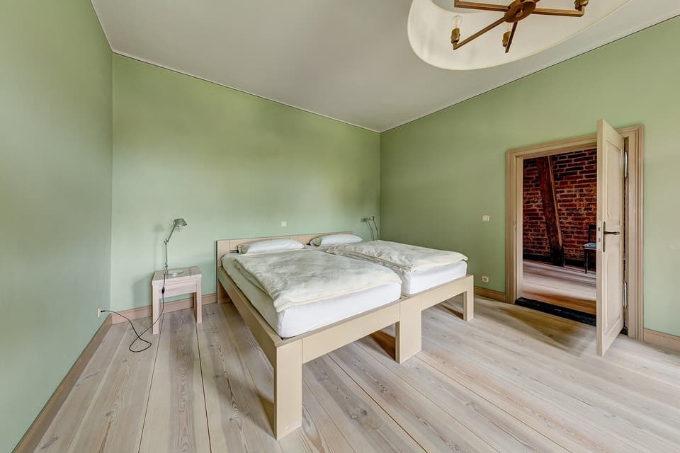 A simple, uncluttered bedroom with light wooden floor and plain walls (illustrative)