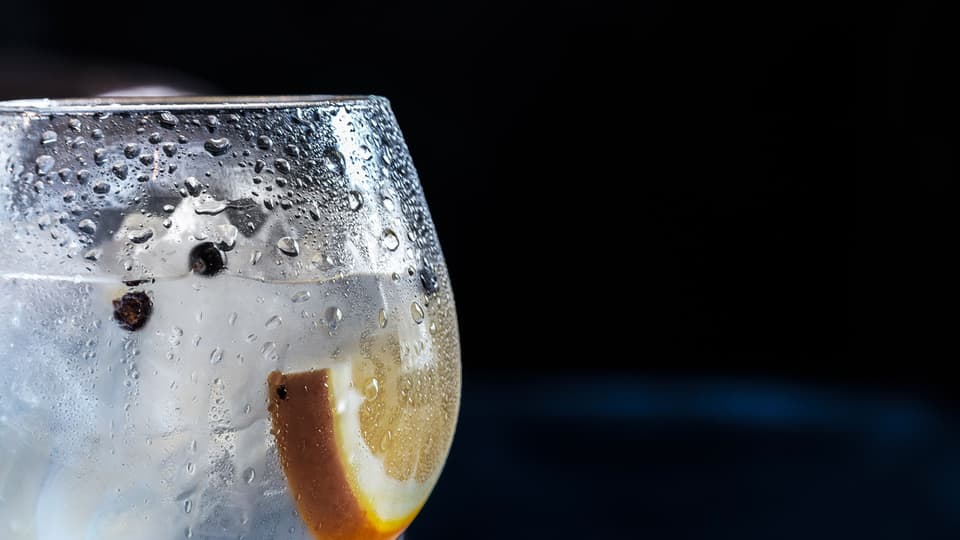 A cold glass with ice and a slice of lemon against a dark background (illustrative)