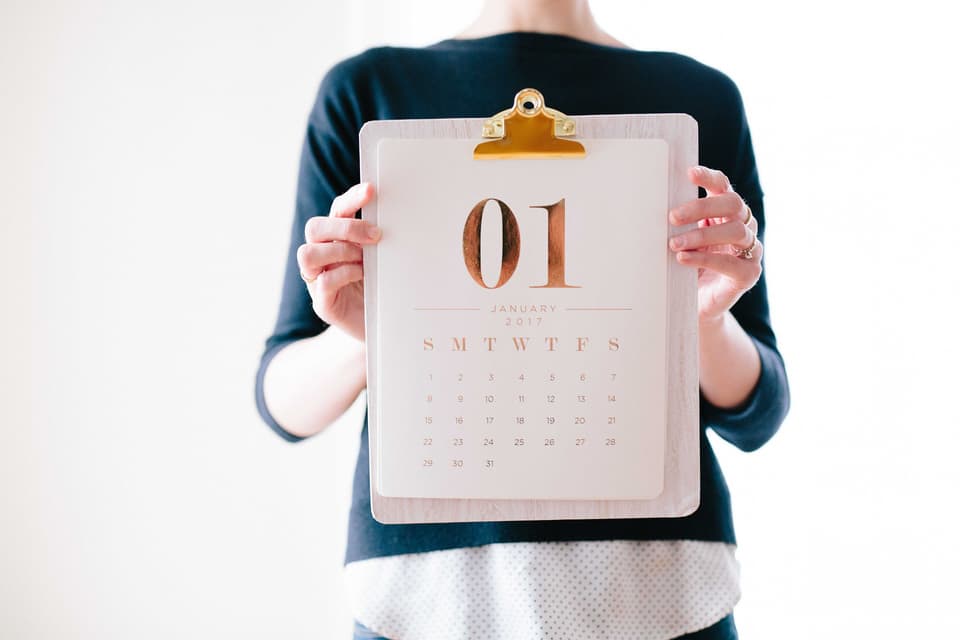 A person holding a January calendar page on a clipboard, face not shown (illustrative)