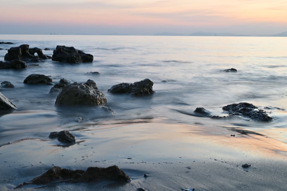 Calm sea washing over rocky shore pools in soft pastel evening light (illustrative)