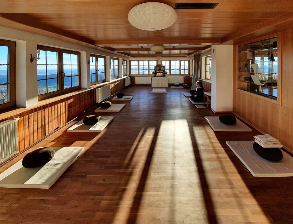 Quiet wooden meditation hall with cushions laid out by the windows (illustrative)