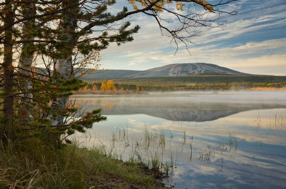A still lake reflecting a fell and trees in morning light (illustrative)