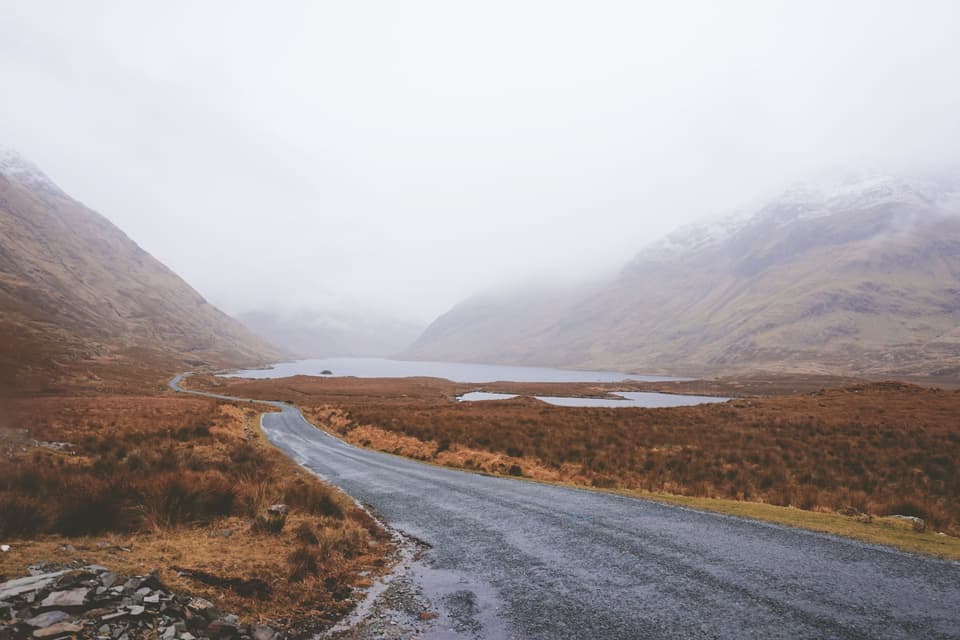 A quiet road winding through a misty valley in the morning (illustrative)
