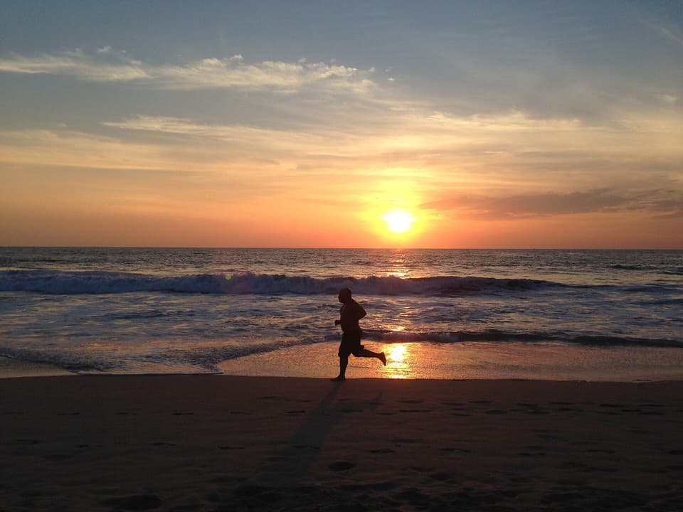 Distant runner silhouetted on the beach at sunrise (illustrative)