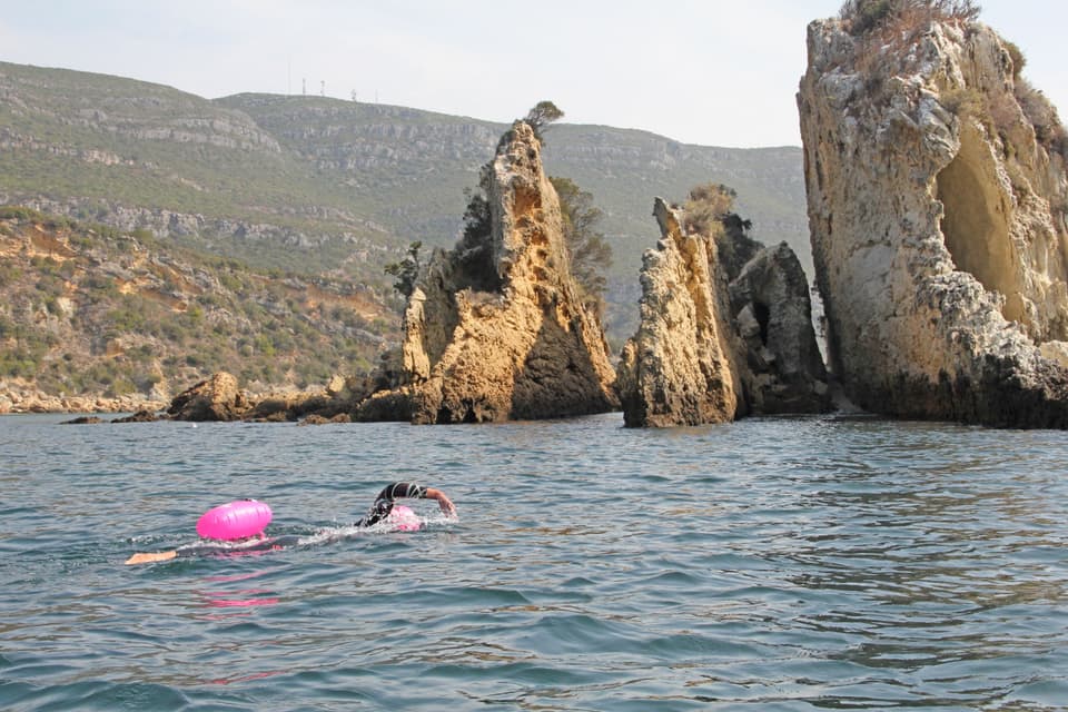 A lone swimmer far out in a calm cove below limestone sea stacks (illustrative)