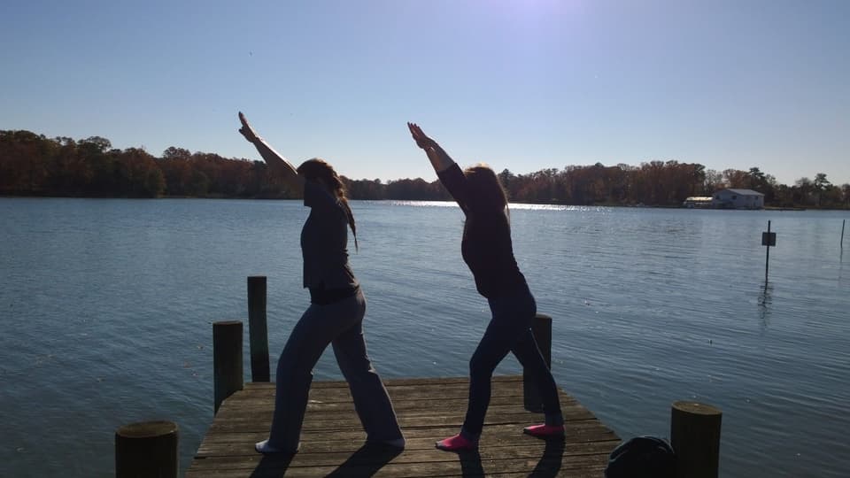 Two people stretching on a wooden jetty by a calm river, in silhouette (illustrative)