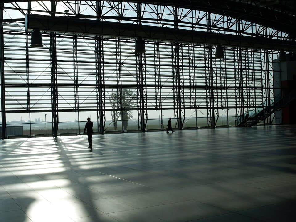 A tall airport window looking out over the apron, a few people in silhouette (illustrative)