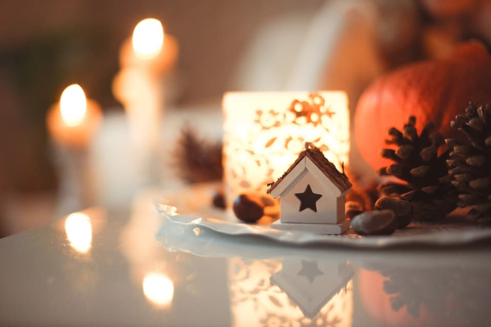 Candles, pine cones and a small wooden house ornament glowing on a table in winter (illustrative)